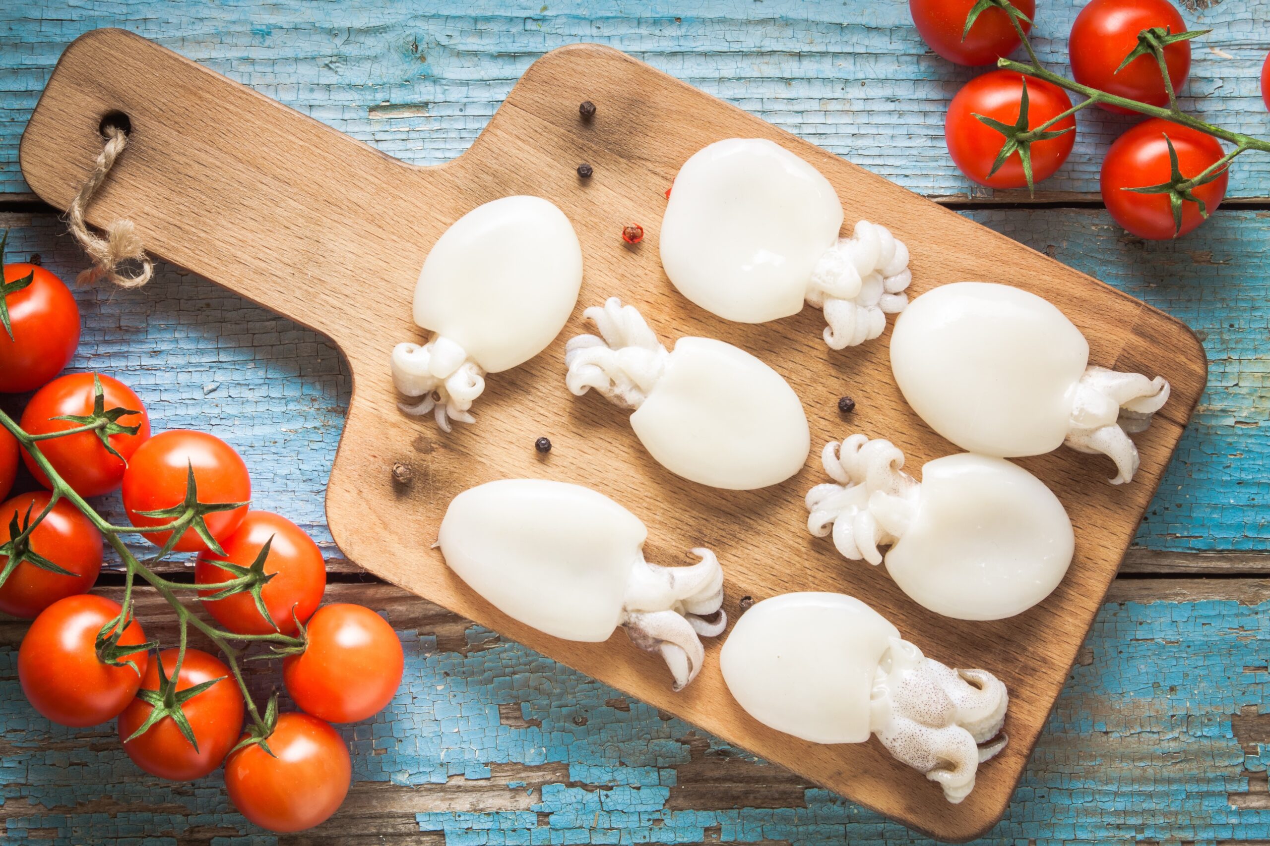 Raw babies cuttlefish on a cutting board with tomatoes
